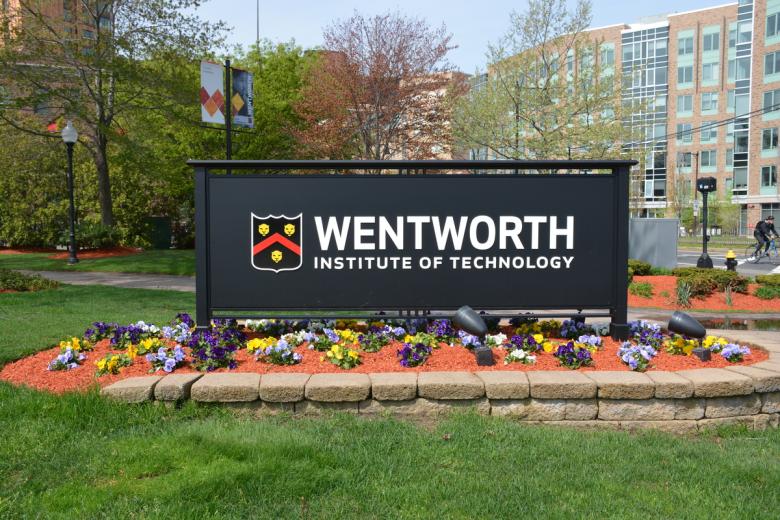 The main Wentworth sign surrounded by flowers at the corner of Ruggles and Huntington Aves